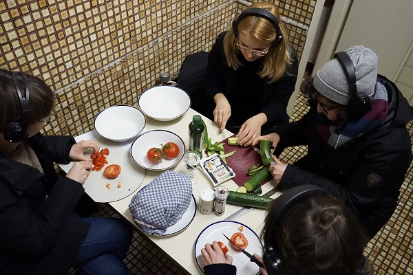 Menschen mit Kopfhörern schneiden gemeinsam Essen an einem Küchentisch